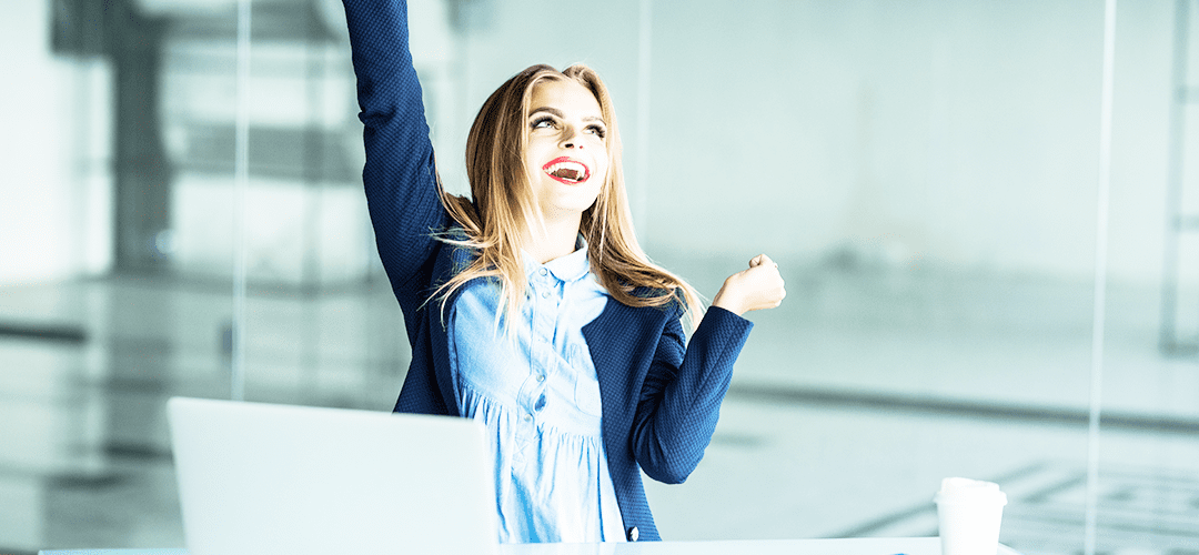 Successful young business woman with arms up at the office