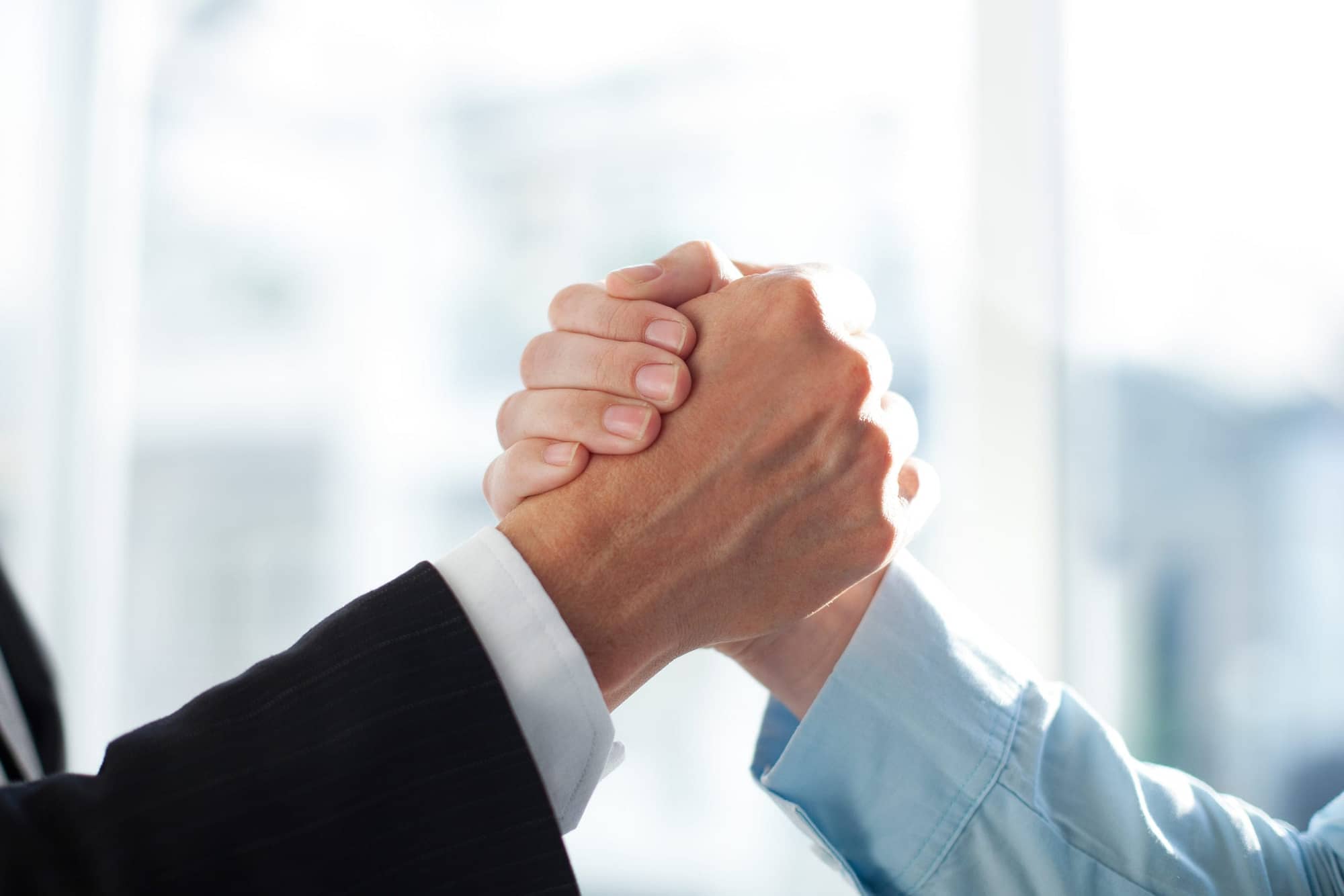 Close-up of two clasped hands of businessmen as sign of strong partnership or team. Unrecognizable men in arm wrestling gesture. Business union concept